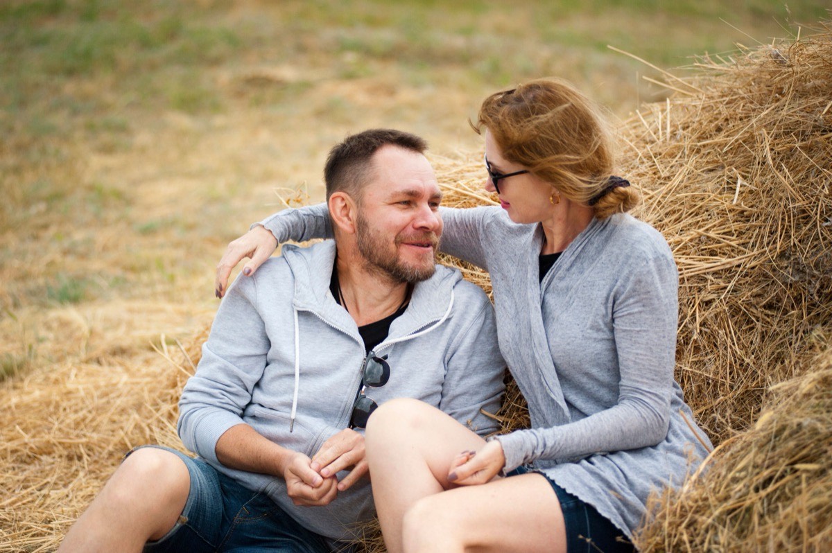 Mature couple smiling together beside a haystack in a field