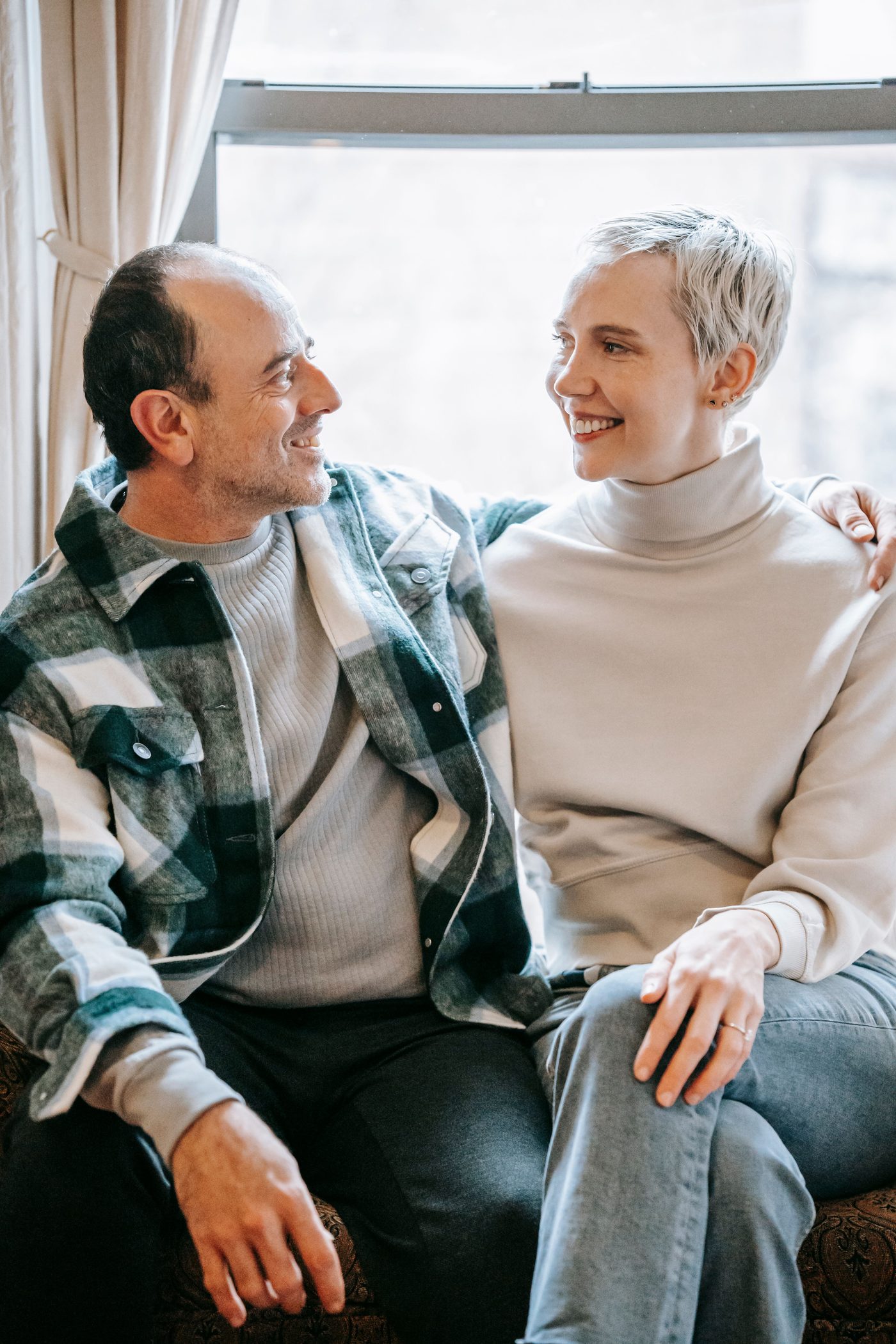 Mature couple smiling together on a sofa by a bright window